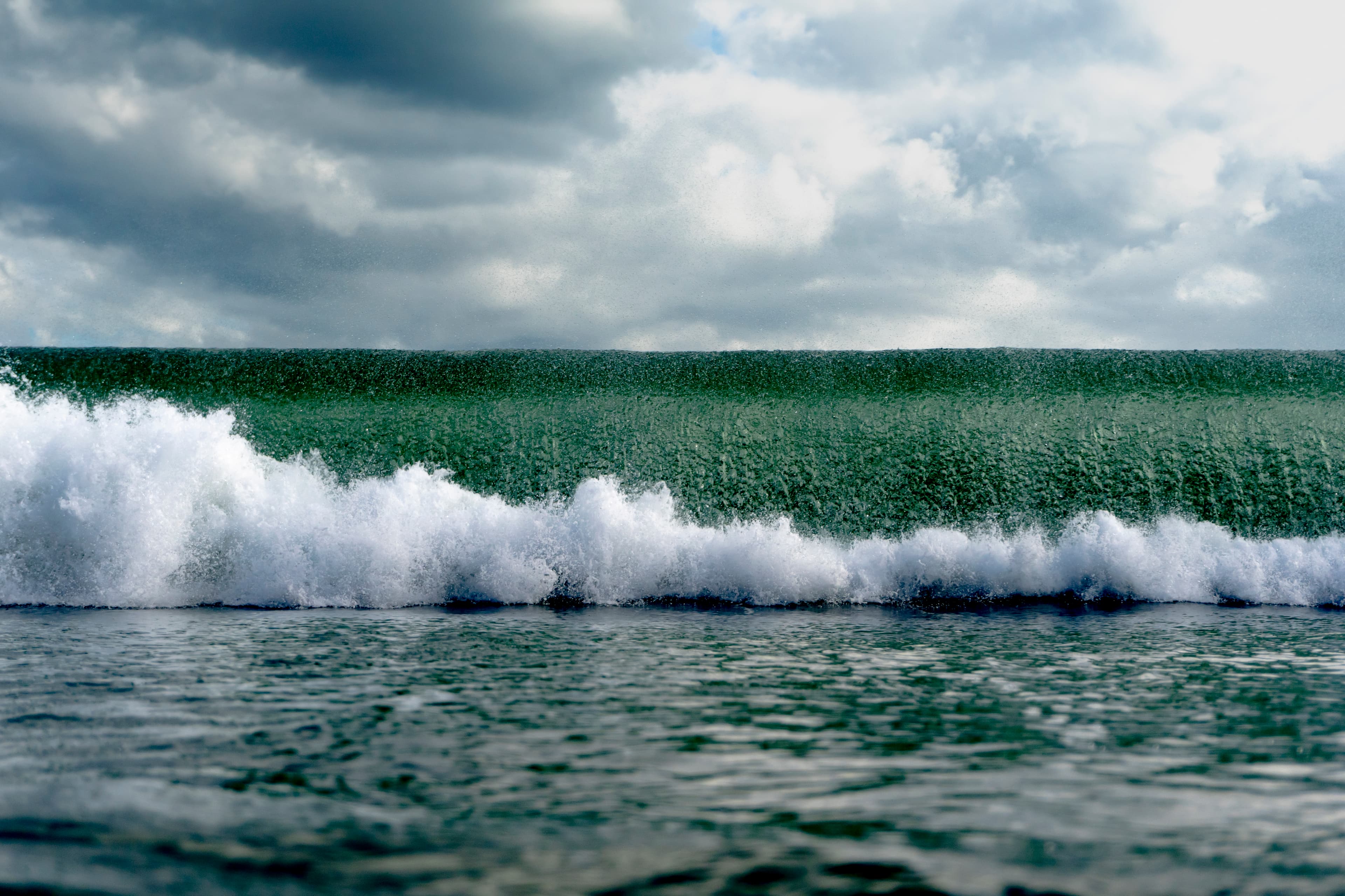 Emerald wave breaking under a stormy sky — fine art ocean photography print, Whangamata NZ.